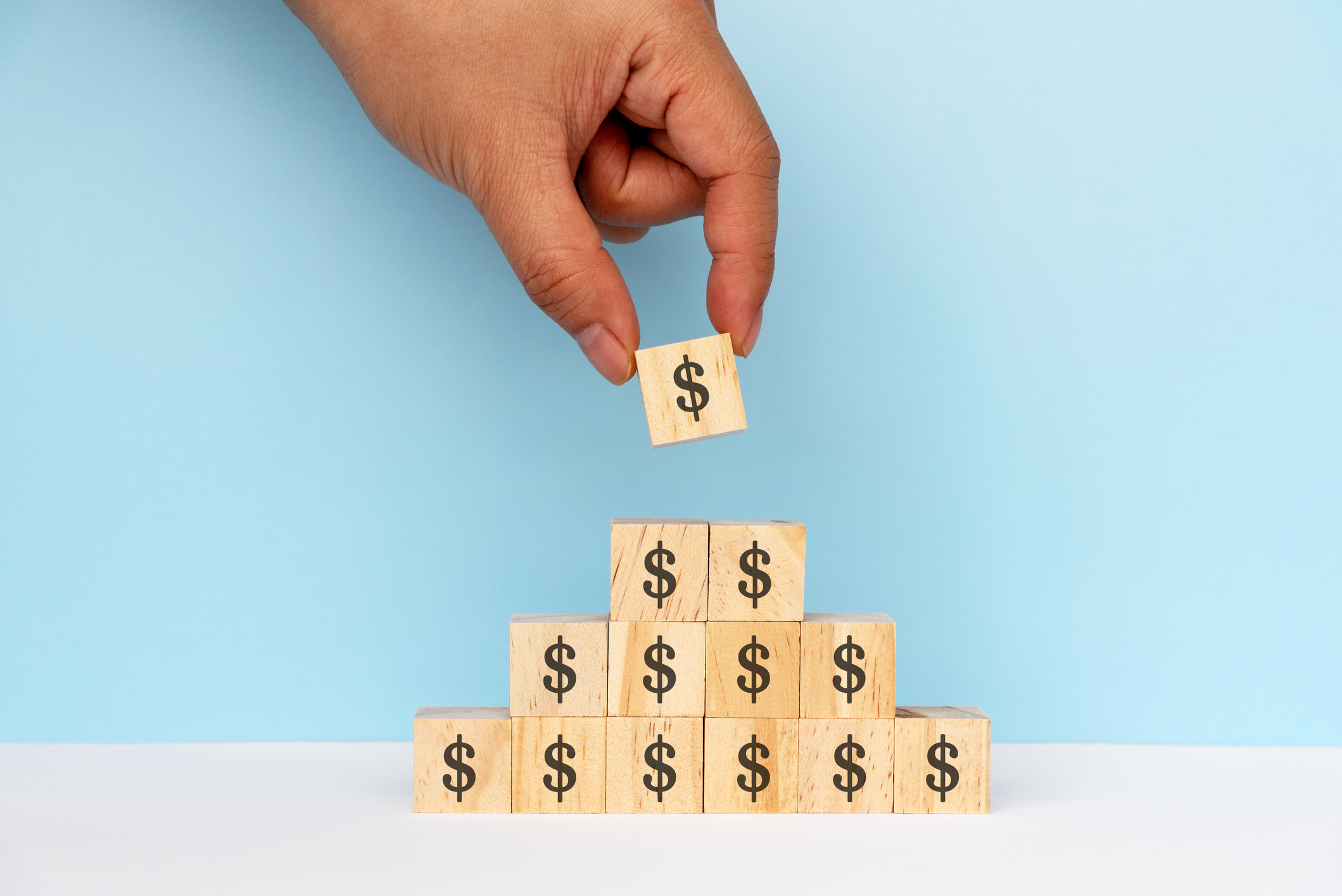 Hands Stacking Dollar Signs on Wood Toy Block
